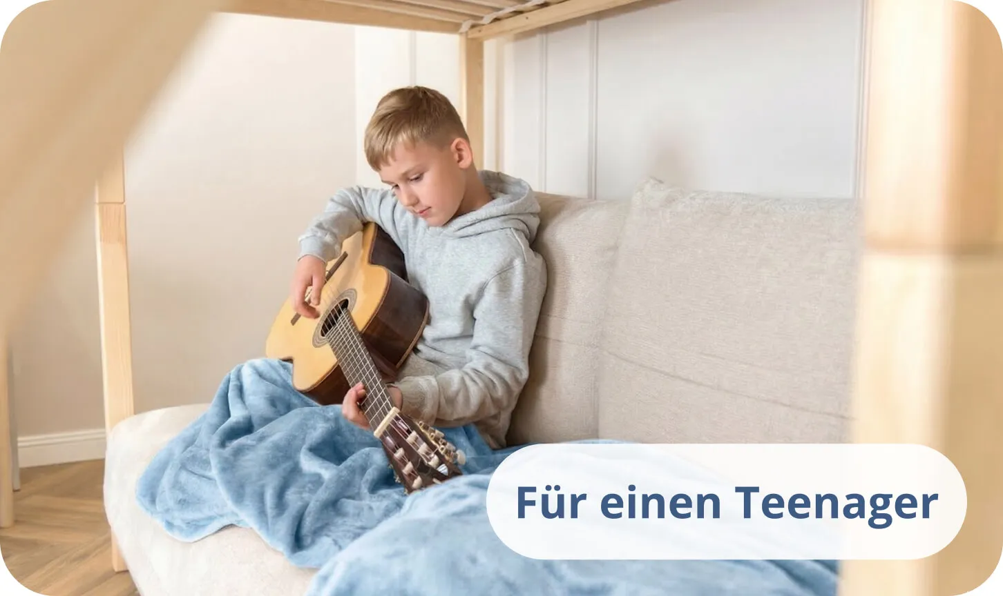 Teenager spielt Akustikgitarre auf einem Bett, bedeckt mit einer blauen Decke.